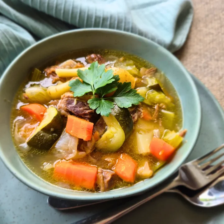 beef and vegetable stew in green bowl with silver knife and fork