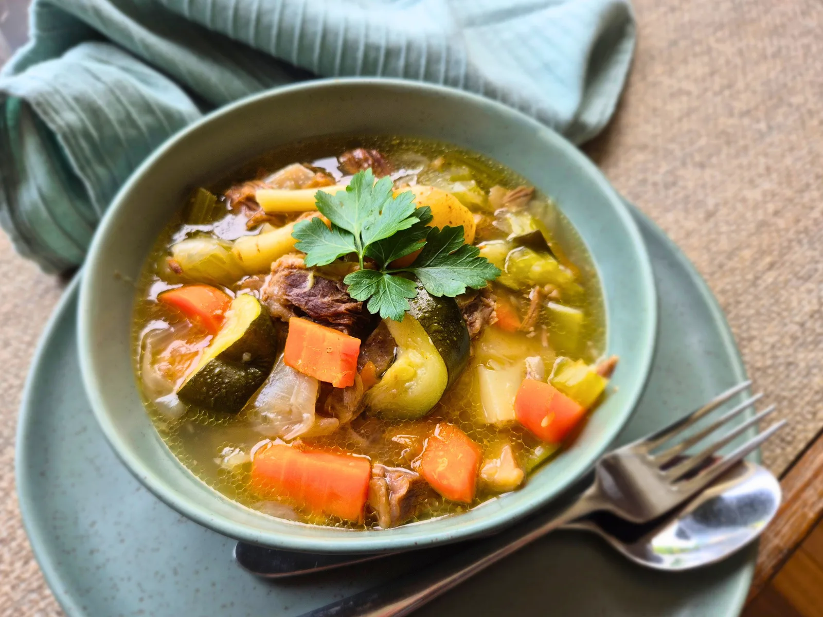 beef and vegetable stew in green bowl with silver knife and fork